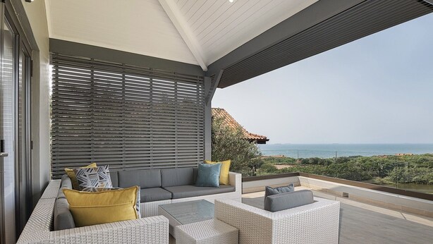 A modern outdoor seating area with wicker furniture and a view of the ocean.