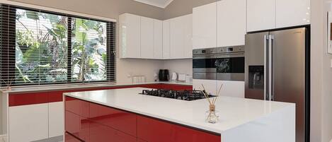 A modern kitchen with a central island, stainless steel appliances, and a view of greenery outside.