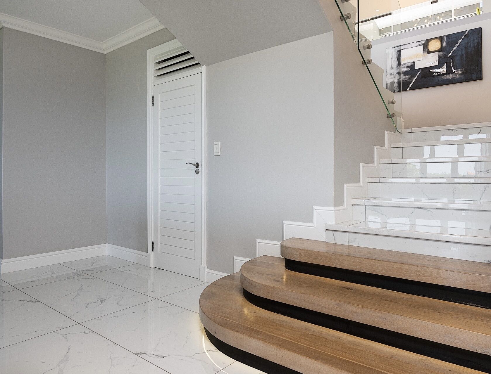 A modern interior with a white door, marble flooring, and a staircase with wooden steps.