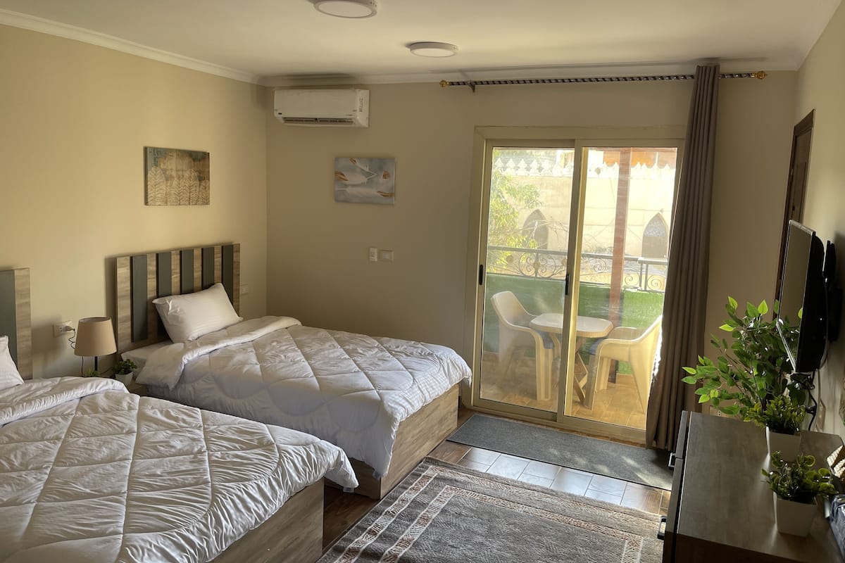 A hotel room with two beds, a balcony with outdoor furniture, and a TV on the wall.
