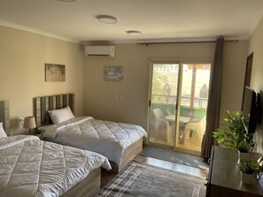 A hotel room with two beds, a balcony with outdoor furniture, and a TV on the wall. - Malek Pyramids Guest House (Giza)