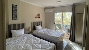 Une chambre d’hôtel avec deux lits, une fenêtre avec des rideaux, un climatiseur fixé au mur et un panneau décoratif.