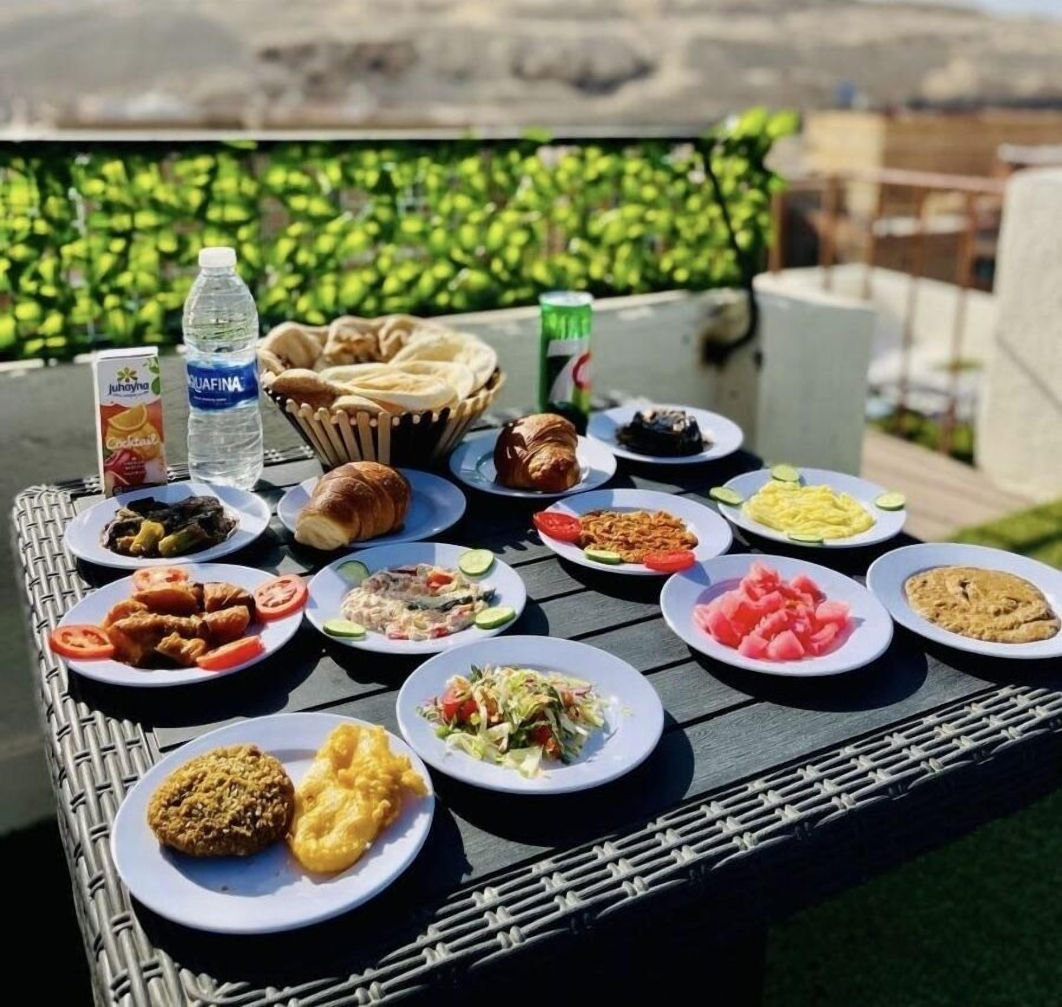 A table set outdoors with various dishes, a bottle of water, and a can of soda.