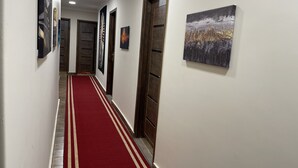Un couloir avec un tapis rouge, des portes en bois et des œuvres d’art encadrées accrochées aux murs.