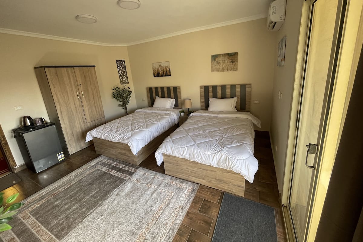 A hotel room with two beds, a desk, a refrigerator, and a door.