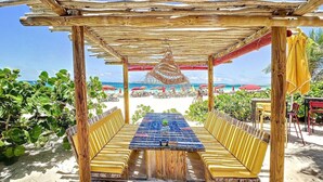 Un espace extérieur aménagé avec des sièges, situé en bord de plage, comprenant une table en bois et des bancs dotés de coussins jaunes.