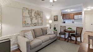 Een woonkamer met een beige bank, een plafondventilator, een eettafel met stoelen, en een keuken met houten kastjes en een magnetron.