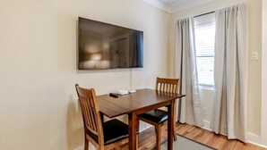 Een eethoek met een houten tafel en stoelen, een flatscreen televisie aan de muur en een raam met gordijnen.