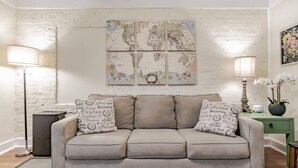 Een woonkamer met een beige bank, twee lampen, een groen bijzettafeltje en een wereldkaart aan de muur.