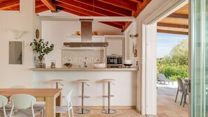 A modern kitchen with a central island, bar stools, and a dining area with a wooden table and white chairs.