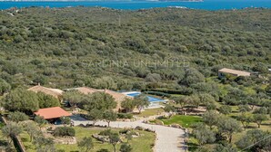 A coastal property with multiple buildings, a swimming pool, and a view of the sea and distant mountains.