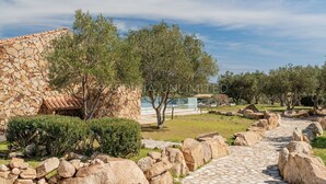 A stone building with a tiled roof, surrounded by olive trees and a stone pathway.