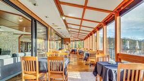 Ein Restaurant mit Holztischen und -stühlen, großen Fenstern und einer Steinwand.