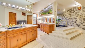 Ein geräumiges Badezimmer mit einem großzügigen Waschtisch, einem beleuchteten Spiegel, Holzschränken und einer Wand mit Natursteinverkleidung.