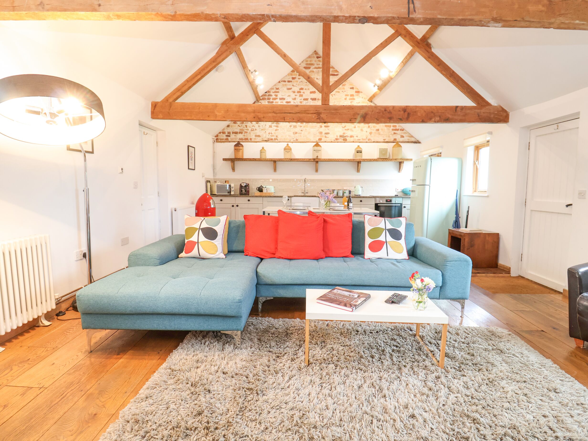 Una sala de estar acogedora con un sofá azul, cojines rojos y multicolores, una mesa de centro blanca y una alfombra mullida.