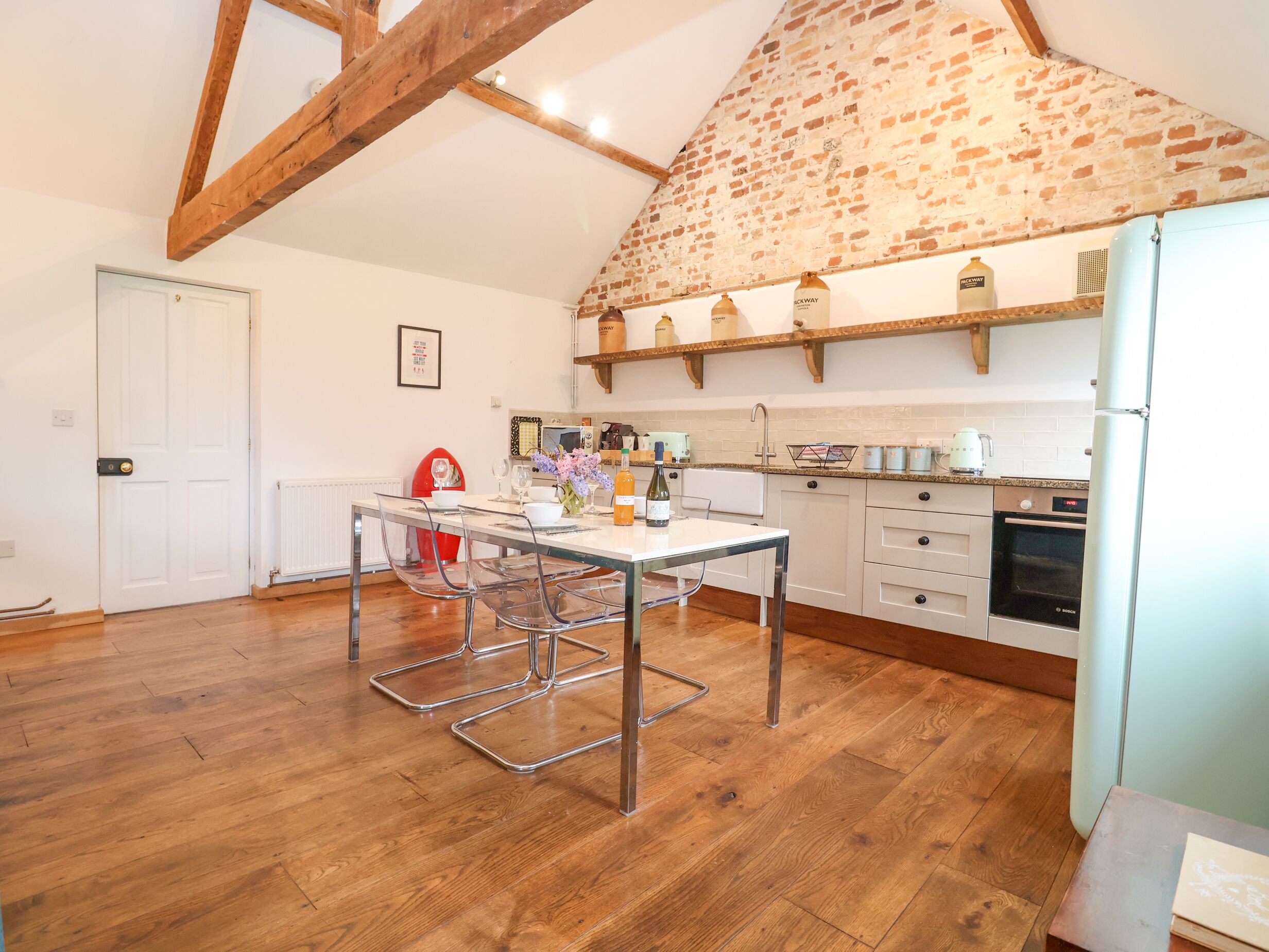 A modern kitchen with wooden beams, a dining area with clear chairs, and a built-in oven.