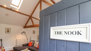 A cozy living room with a blue door labeled "THE NOOK," a gray sofa, a coffee table, and a guitar. - The Nook (Halesworth)