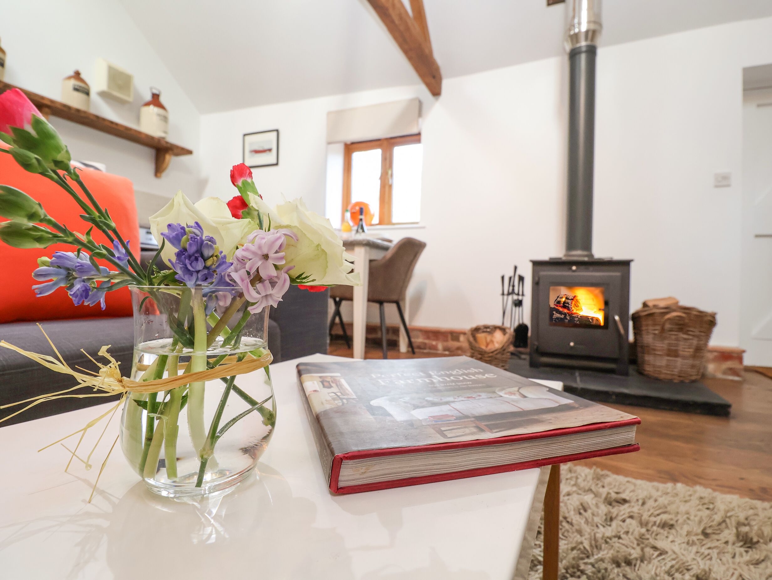 A living room with a glass vase of flowers, a red book, a sofa, a fireplace, and a dining area.