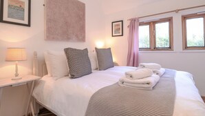 A neatly made bed with pillows, a bedside table with a lamp, and a window with curtains. - The Nook (Halesworth)