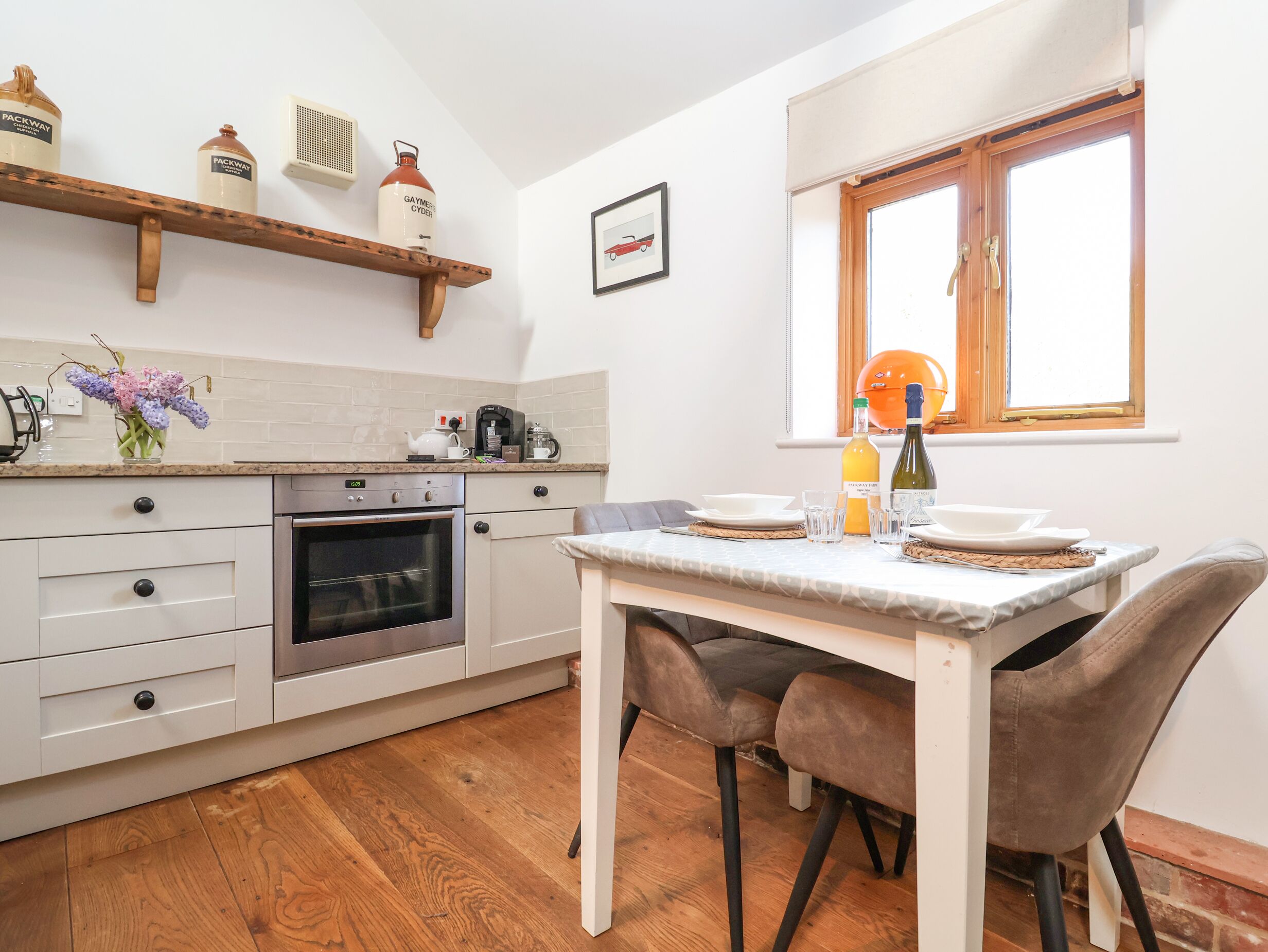 Una cocina compacta con horno integrado, cafetera y una pequeña mesa de comedor con sillas.