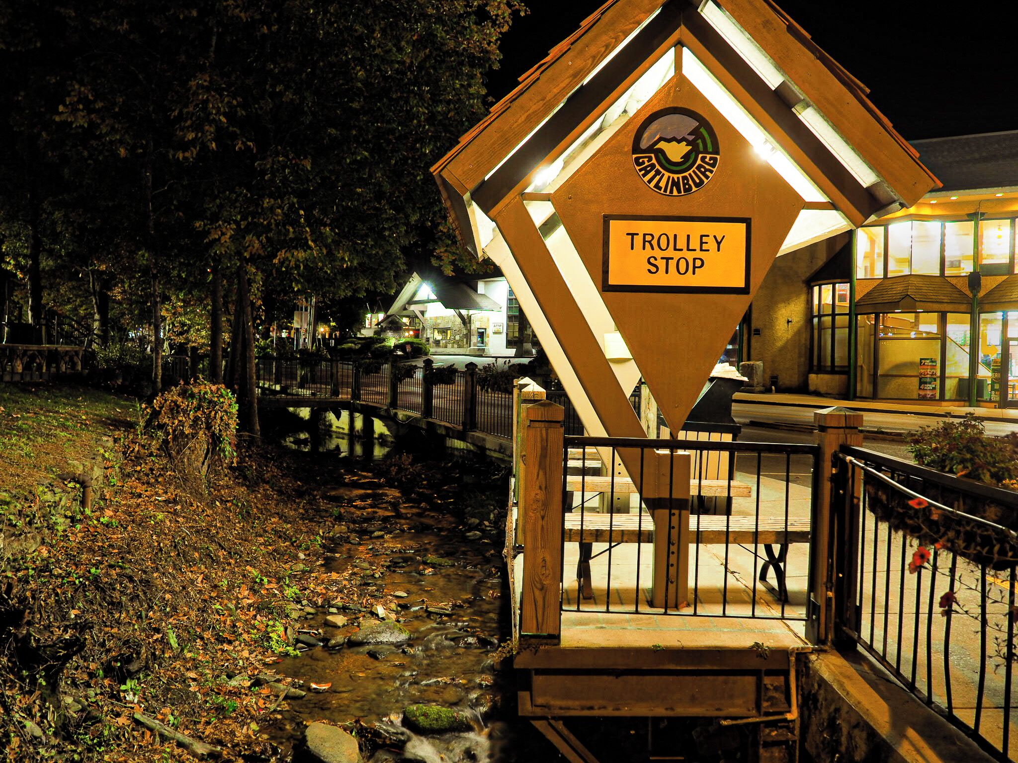 A trolley stop sign with a logo, surrounded by a wooden fence and a stone pathway.