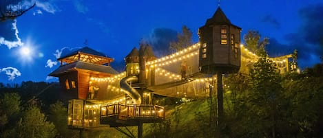 A treehouse with a rope bridge, surrounded by greenery and a night sky.