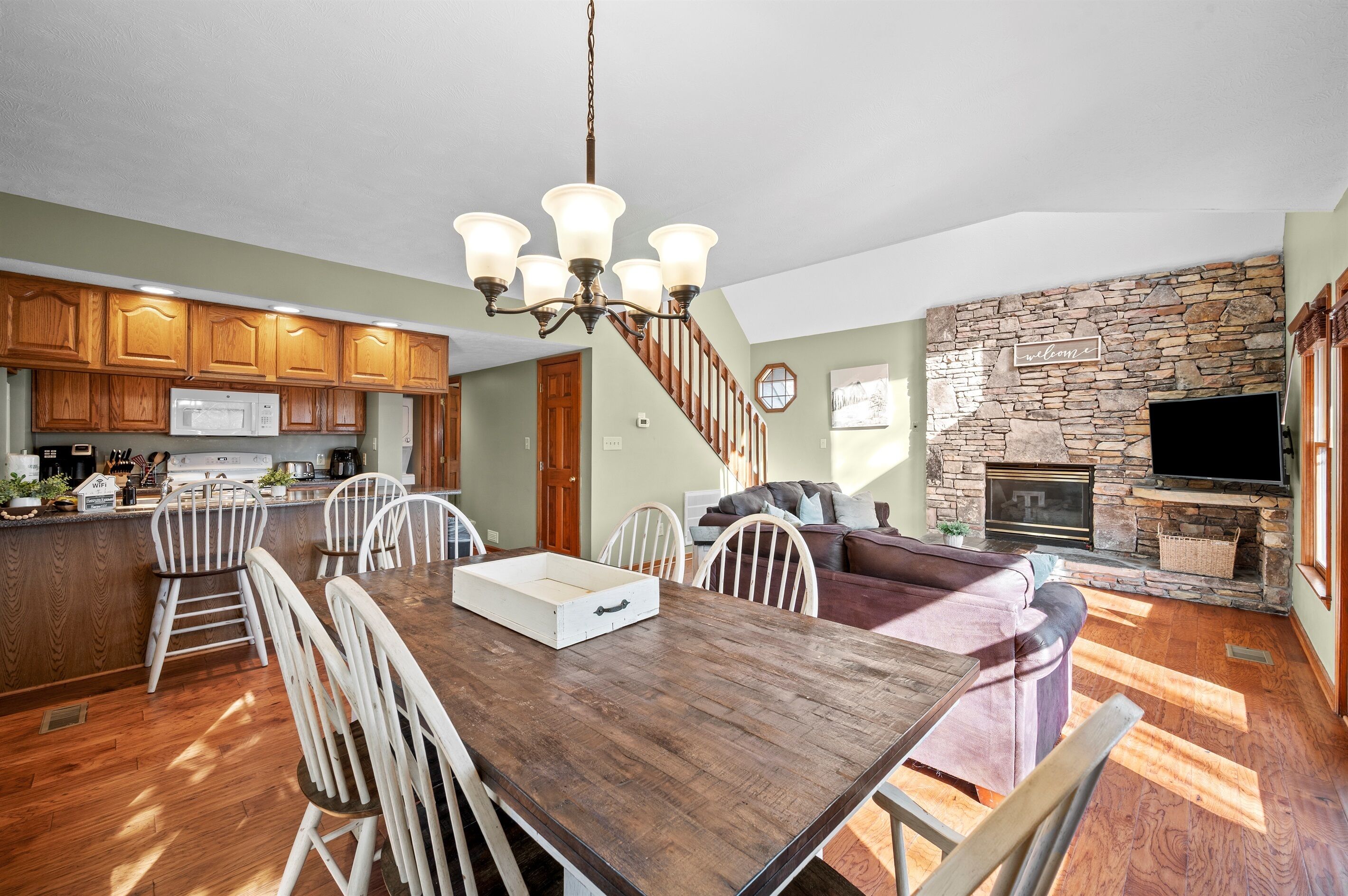 A spacious kitchen with wooden cabinets, a dining area with a wooden table and chairs, a stone fireplace, and a cozy seating area with a sofa.