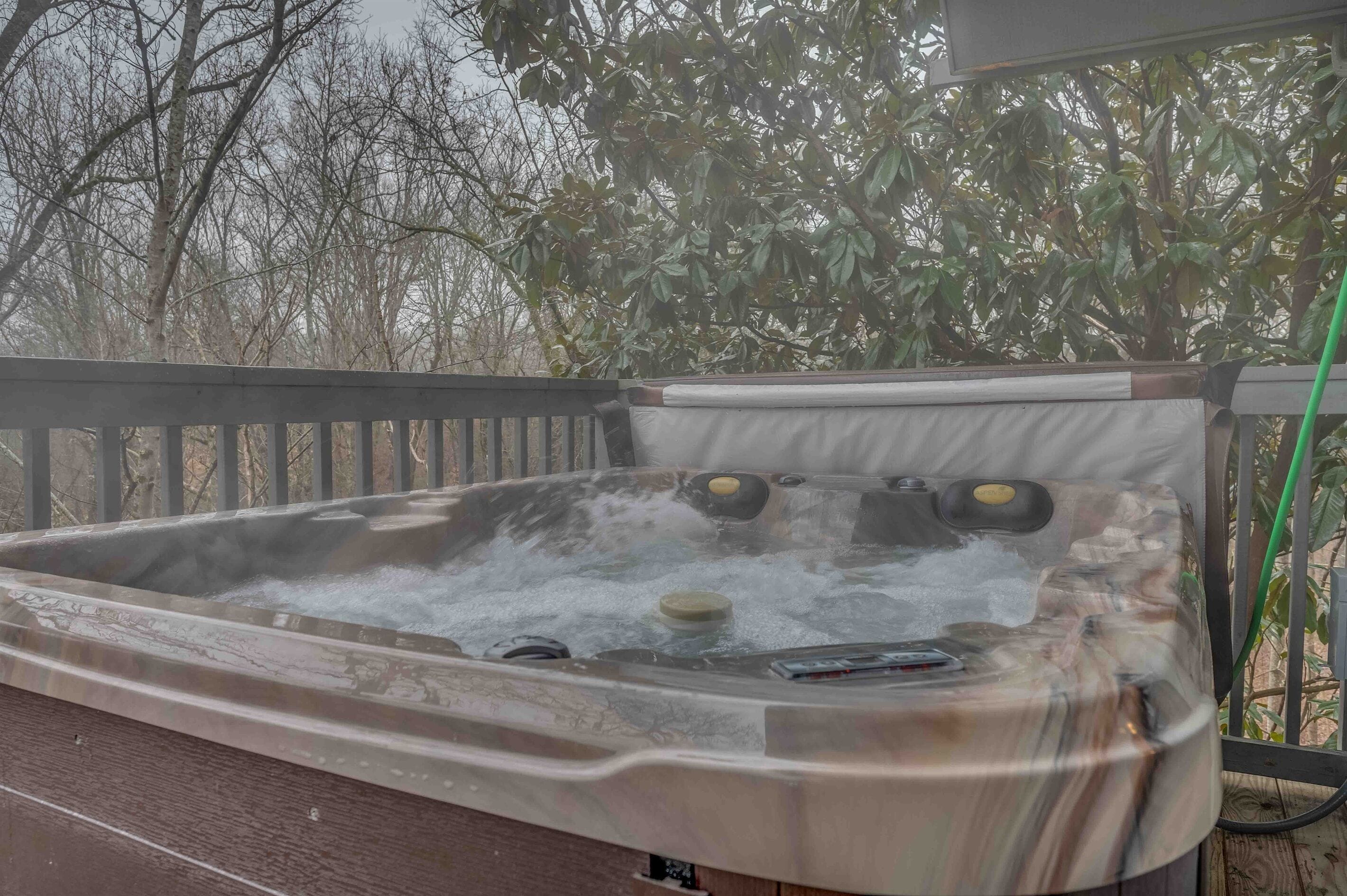 A hot tub with multiple jets, surrounded by a wooden deck and trees.