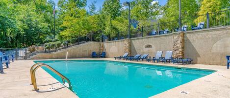 A swimming pool with a stone wall and lounge chairs.