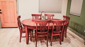 A dining area with a round wooden table and six chairs, a basket with bread, and a closed wooden door.