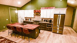 A compact kitchen with white cabinets, a stainless steel refrigerator, and a wooden island with bar stools.