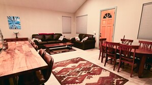 A living room with a wooden dining table, leather sofas, a patterned rug, and a door with a window.