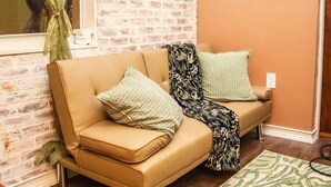 Un salon chaleureux avec un mur en briques, un téléviseur à écran plat, un canapé beige et un tapis à motifs.