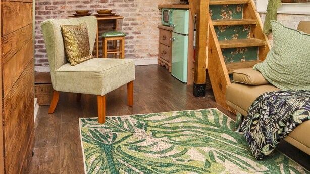 Un salon chaleureux avec un lit en mezzanine, un fauteuil vert, un tapis à motifs et un réfrigérateur de style rétro.