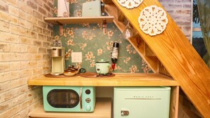 Une cuisine équipée d’un four à micro-ondes de style rétro, d’un petit réfrigérateur et d’une étagère en bois où sont rangés des ustensiles de cuisine.
