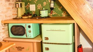 Une cuisine avec un réfrigérateur turquoise d’époque, une étagère en bois ornée d’objets décoratifs et un mur en briques.