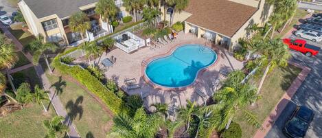 An aerial view of a hotel with a swimming pool, palm trees, and a parking lot.