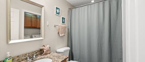 Une salle de bain avec un lavabo à vasque en granit, des toilettes blanches et un rideau de douche.