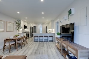 Una cocina moderna con armarios blancos, una isla central con taburetes y una zona de comedor con mobiliario de madera.