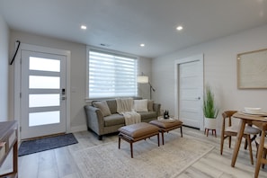 Una sala de estar moderna con un sofá gris, una mesa de centro de madera y un comedor con una mesa y sillas de madera.