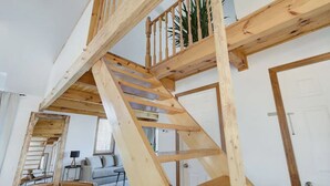 Un vaste espace de vie de style « loft », avec des poutres apparentes, un escalier en bois et une vue sur un balcon.