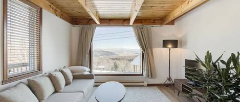 A cozy living room with a wooden ceiling, a sofa, a small table, a lamp, and a potted plant.