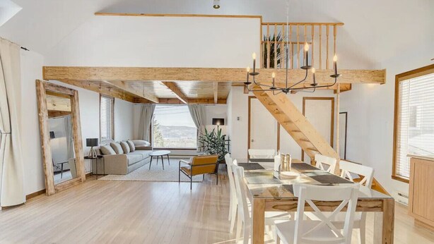 Un vaste espace de vie agrémenté d’un escalier en bois, d’une table à manger avec des chaises et d’une grande fenêtre offrant une vue sur l’extérieur.