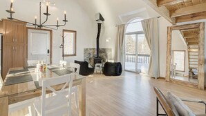 Un vaste espace de vie comprenant une table à manger en bois, des chaises blanches, un canapé noir et une cheminée.