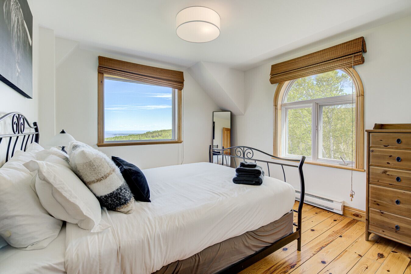 Une chambre à coucher avec un lit, une commode et deux fenêtres donnant sur un beau paysage.