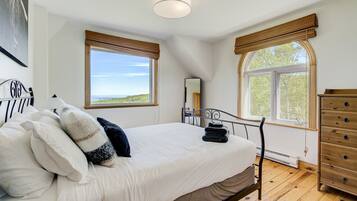 Une chambre à coucher avec un lit, une commode et deux fenêtres donnant sur un beau paysage.