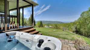 Un bain à remous dans un jardin, avec une terrasse en bois, un espace salon abrité et une vue sur le paysage environnant.