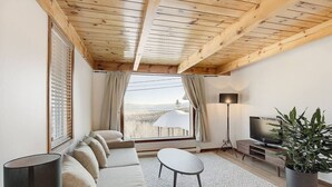 Un salon moderne avec un plafond en bois, un canapé, un téléviseur, une lampe et une vue sur un paysage.