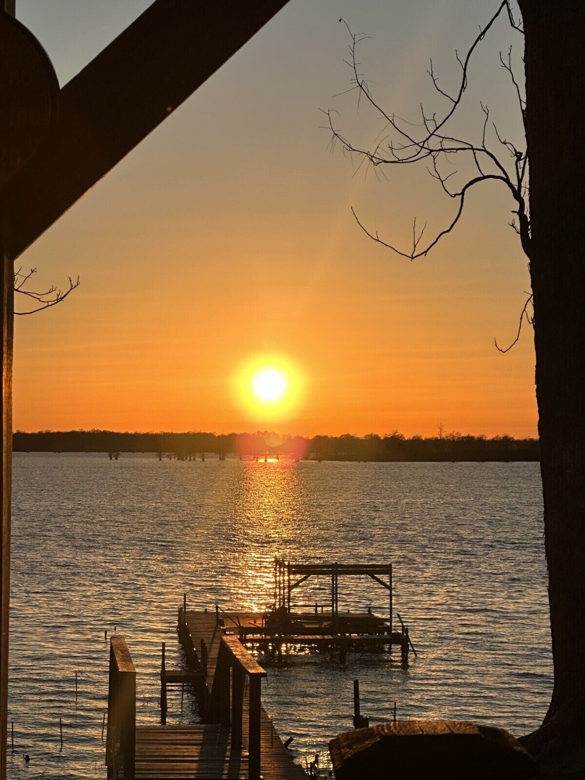 A sunset over a calm lake with a wooden dock extending into the water.