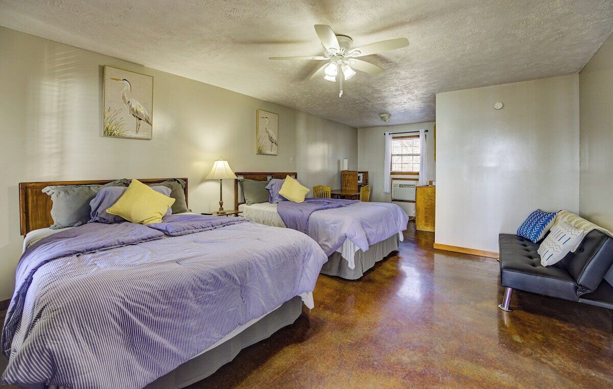A hotel room with two beds, a ceiling fan, a sofa, and artwork on the walls.